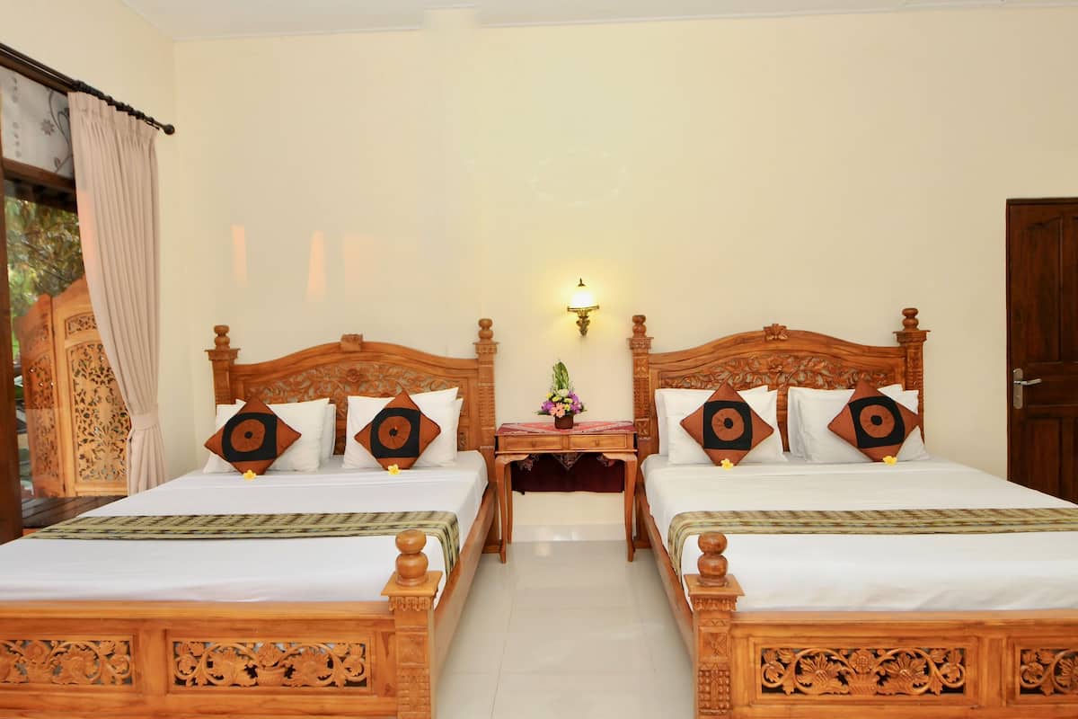 A hotel room with two wooden beds, a nightstand with a lamp, and a decorative wall panel.