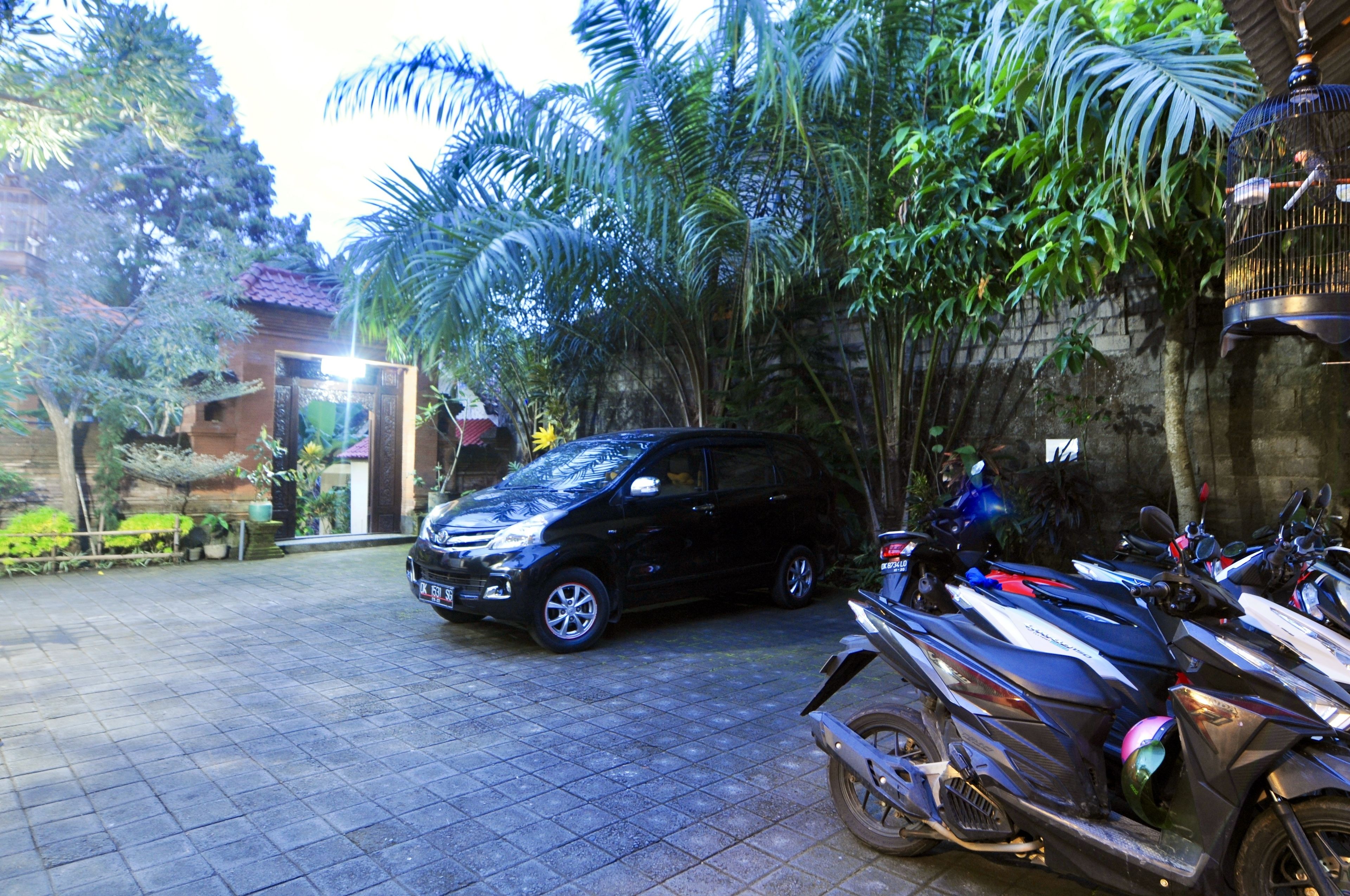A black car parked in a driveway with a motorcycle and a birdcage on the right.