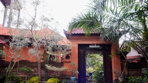 A traditional building with a red-tiled roof, a wooden gate, and a variety of potted plants and trees. - Rahayu 2 Bungalows (Ubud)