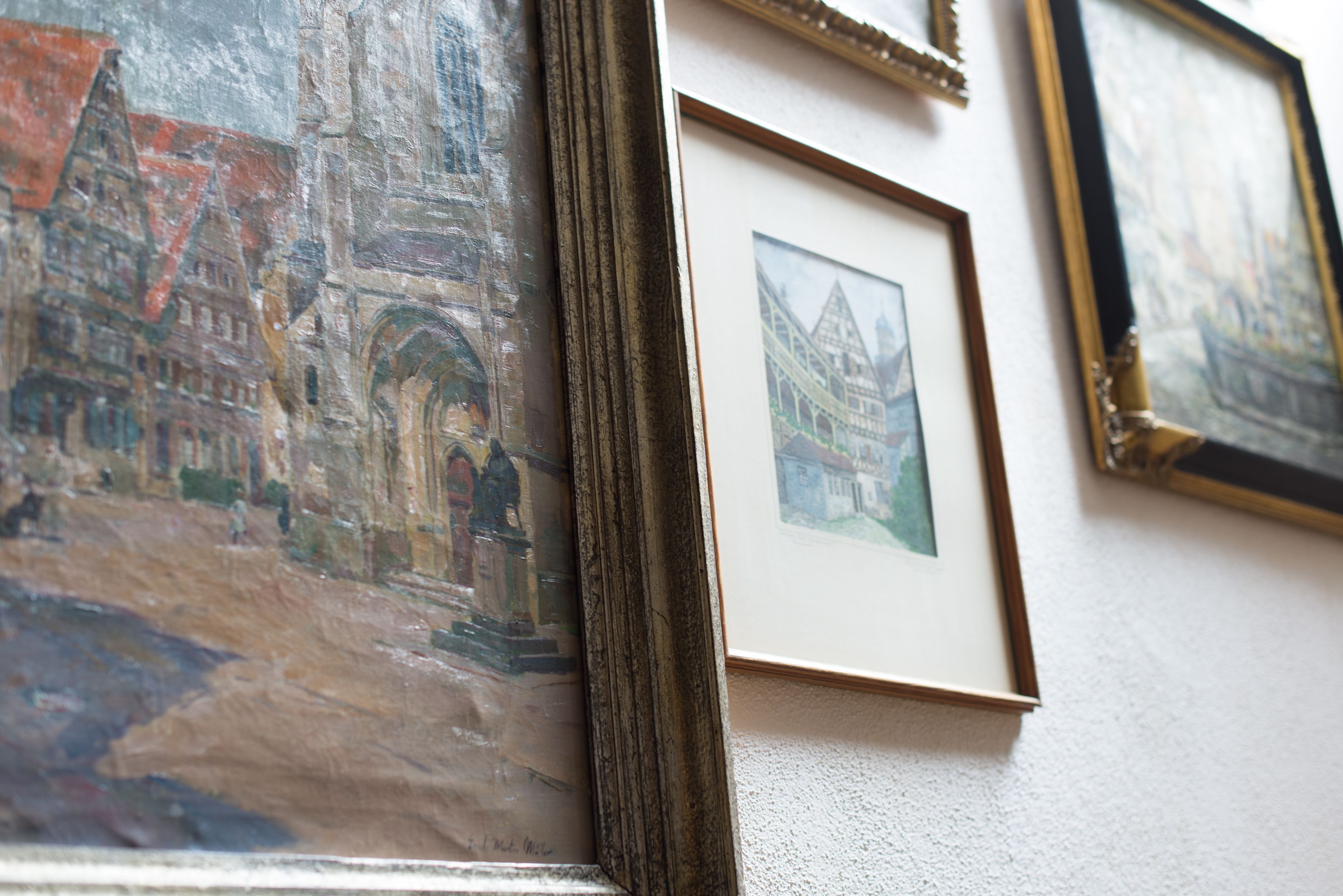 A wall with multiple framed artworks, including a painting of a historical building and a smaller framed picture.