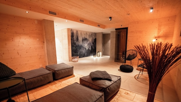 Un intérieur moderne avec des murs en bois, une grande peinture représentant une forêt et un coin salon agrémenté de coussins et d’un fauteuil.