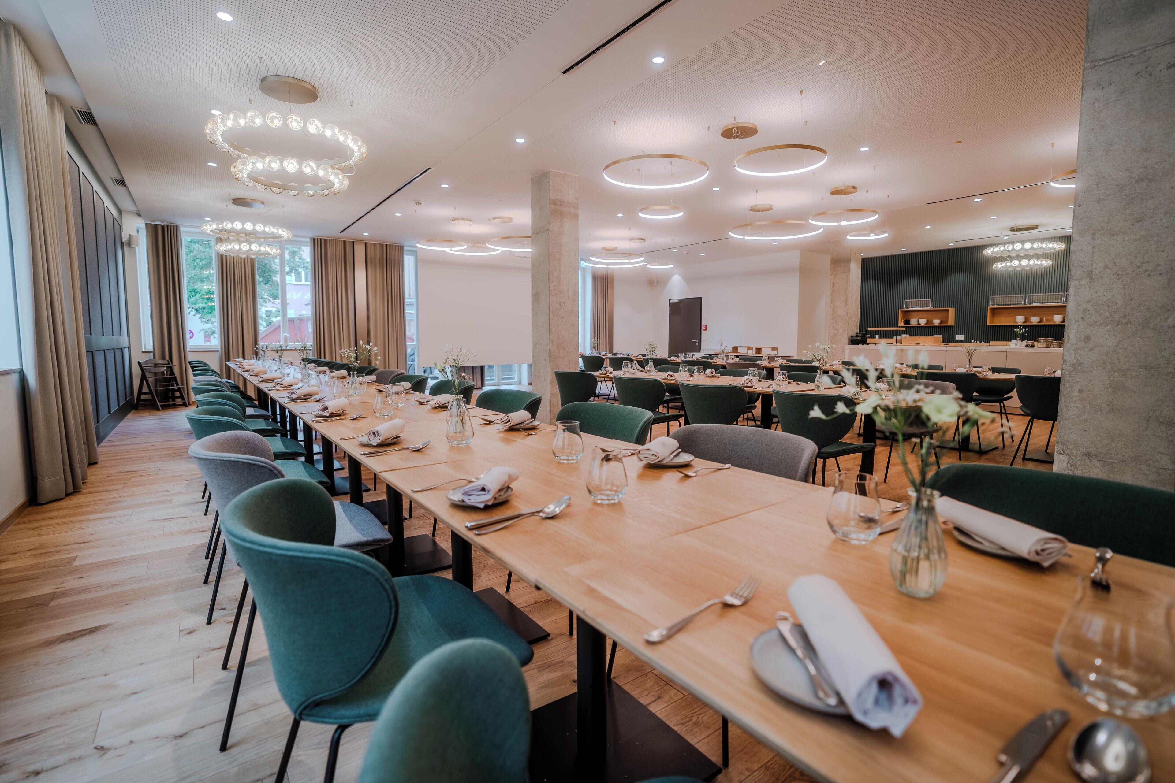 Un comedor amplio con mesas largas, sillas verdes y luminarias modernas.