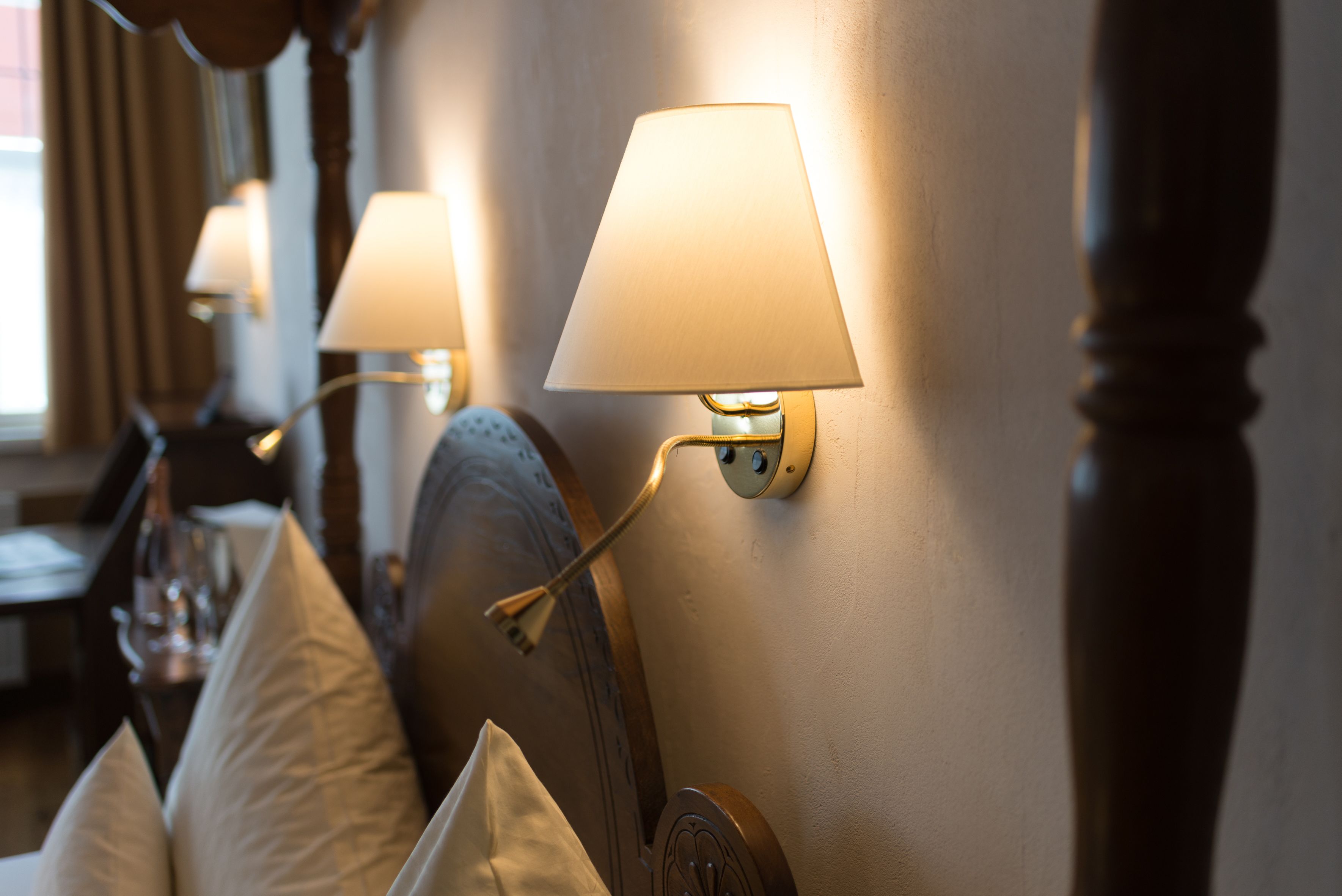 A hotel room with a bed, a nightstand, and a wall-mounted lamp.