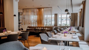 Un restaurant moderne avec de longues tables, des chaises grises et un panneau décoratif en bois au fond.