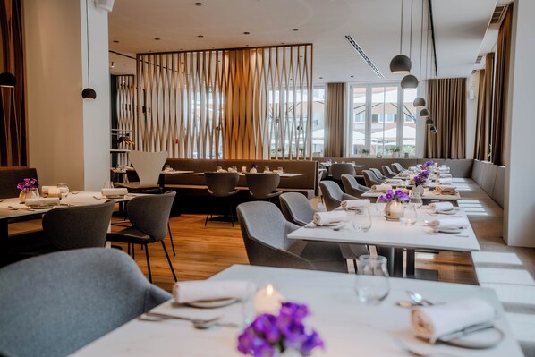 Un restaurant moderne avec de longues tables, des chaises grises et un panneau décoratif en bois au fond.