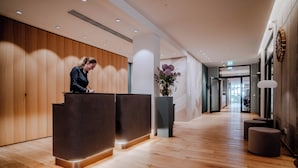 Un espace d’accueil moderne avec un plancher en bois, deux comptoirs d’accueil de couleur sombre et un vase rempli de fleurs violettes.