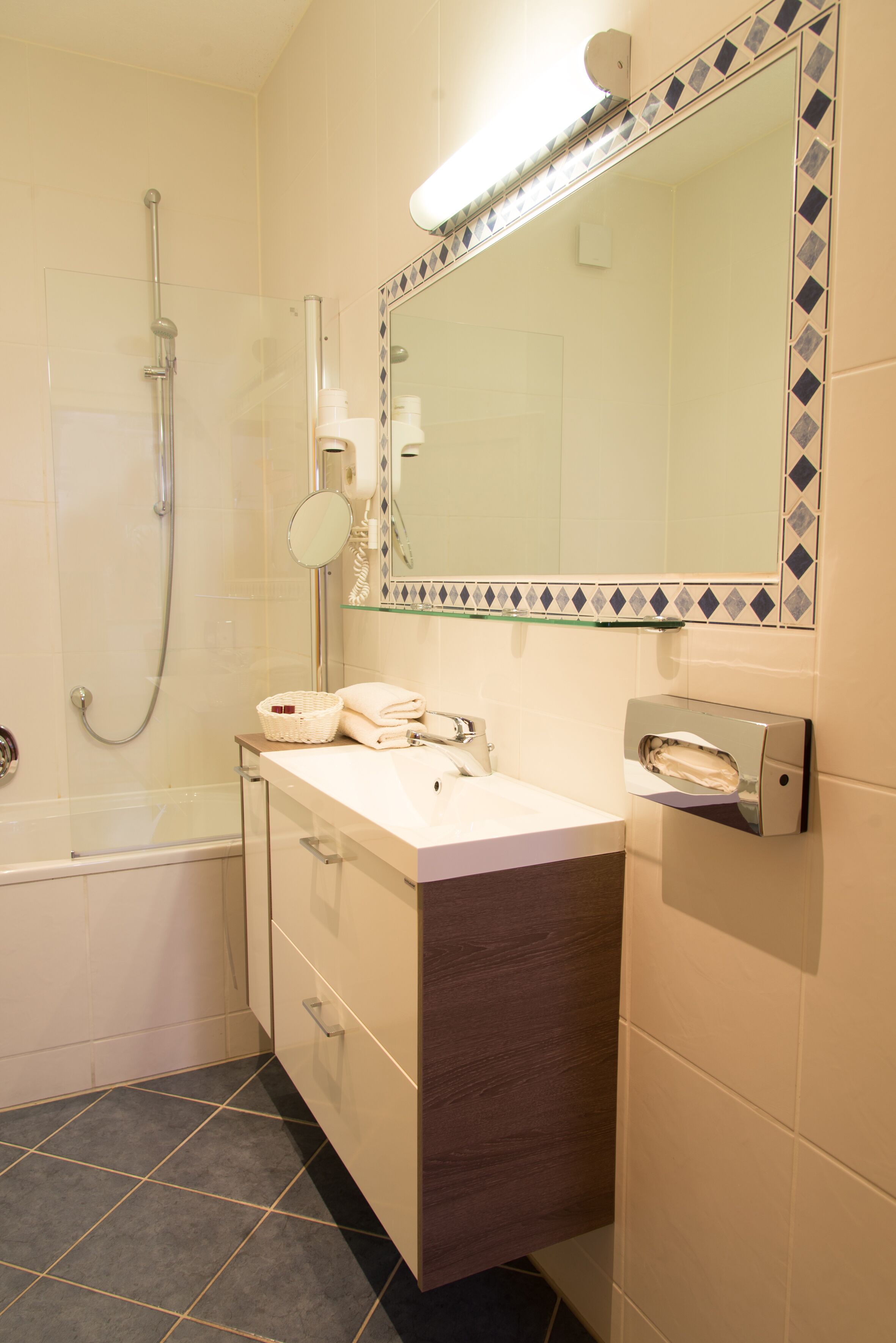 A modern bathroom with a glass-enclosed shower, a vanity with a mirror, and a towel dispenser.