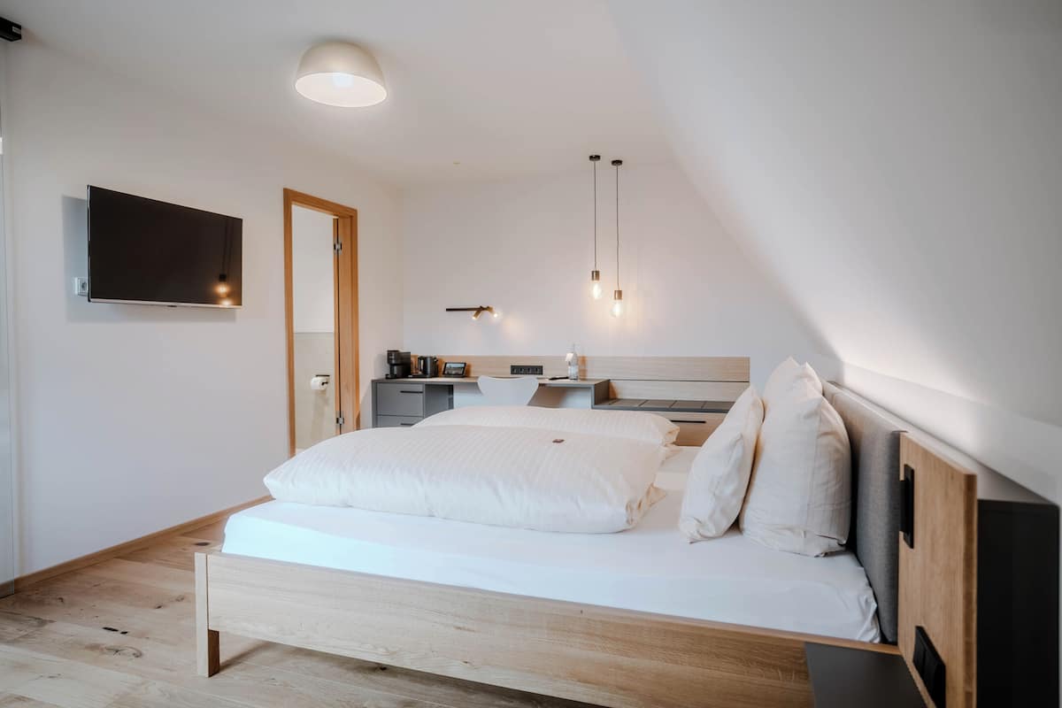 A modern bedroom with a wooden bed, a desk, a chair, and a TV mounted on the wall.