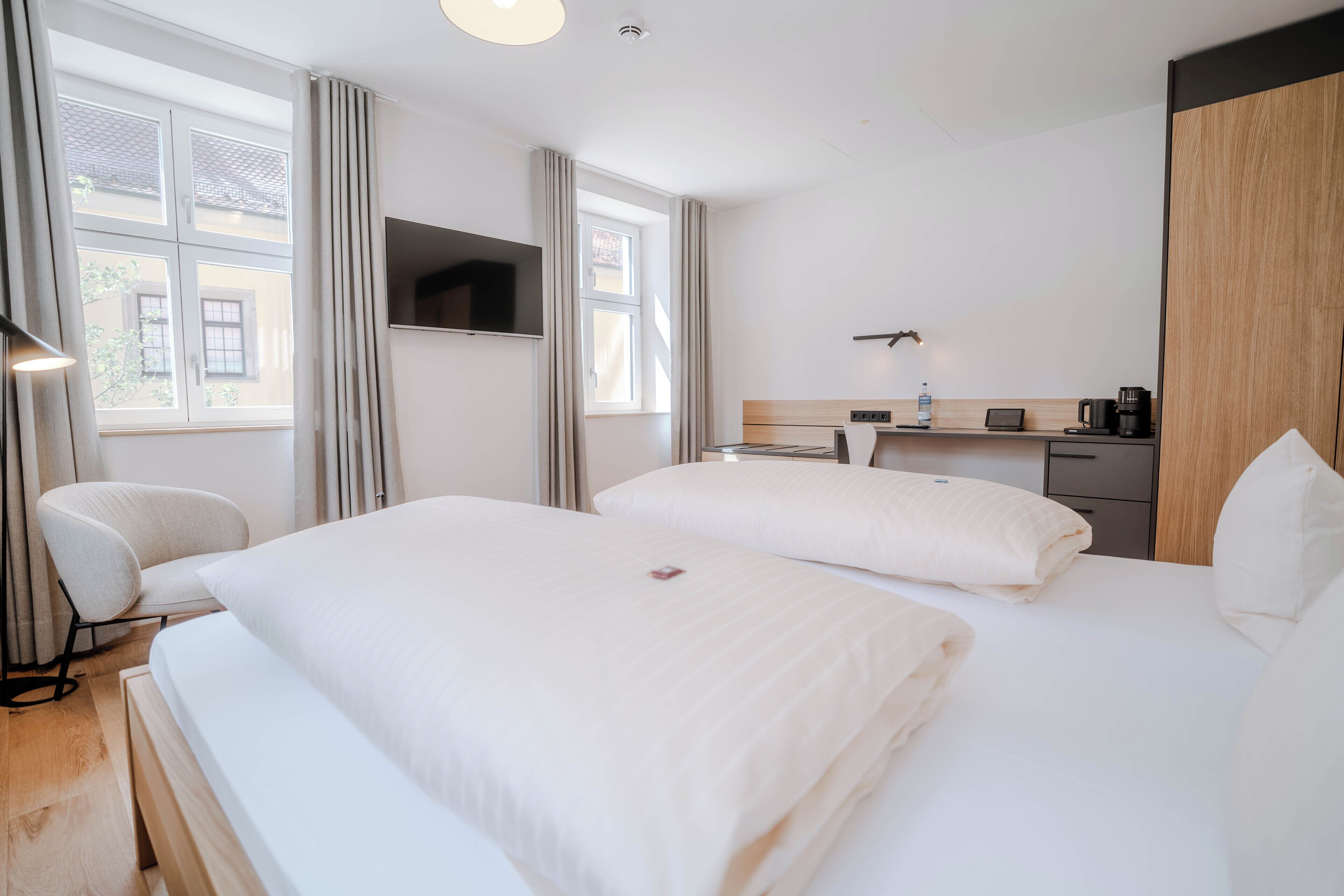 Een hotelkamer met twee bedden, een bureau, een stoel, een televisie en een raam met gordijnen.