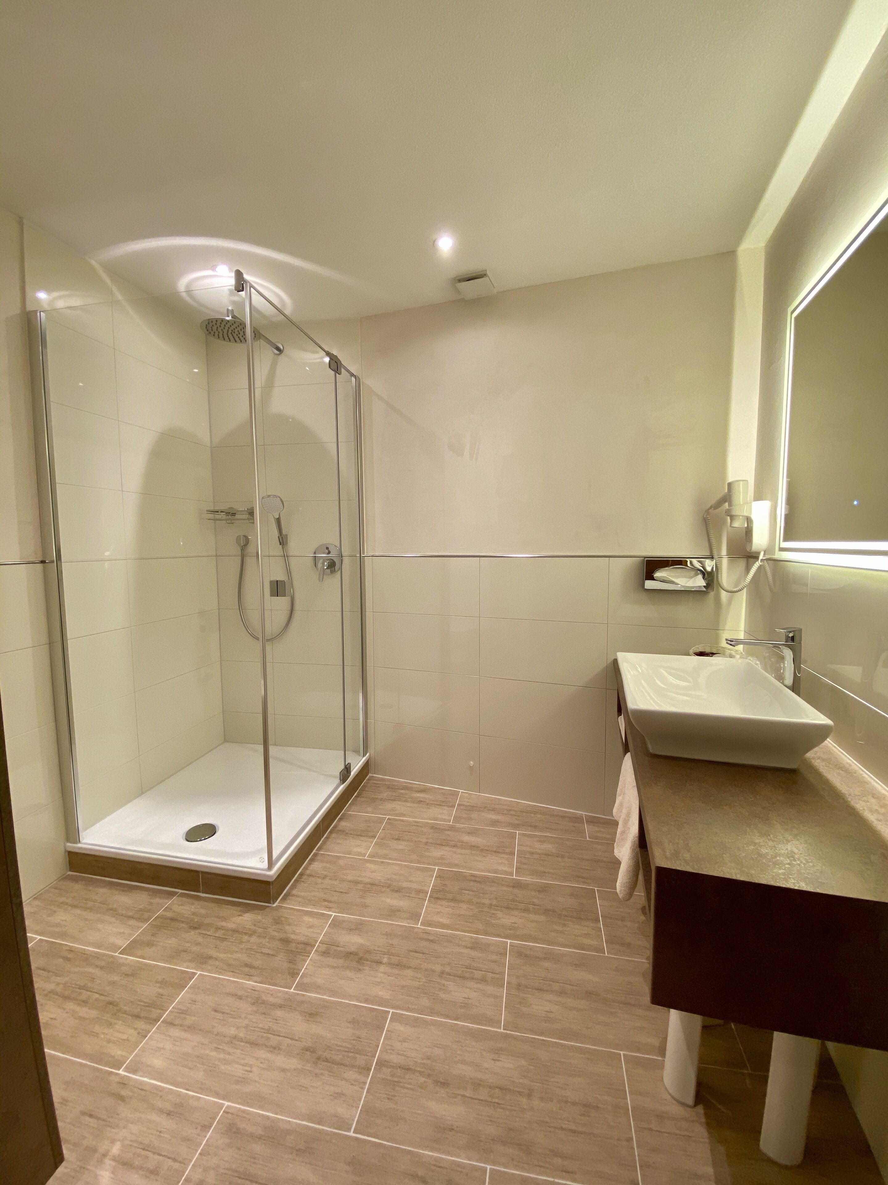 Un baño moderno con ducha de vidrio, lavamanos con espejo y suelo de baldosas.