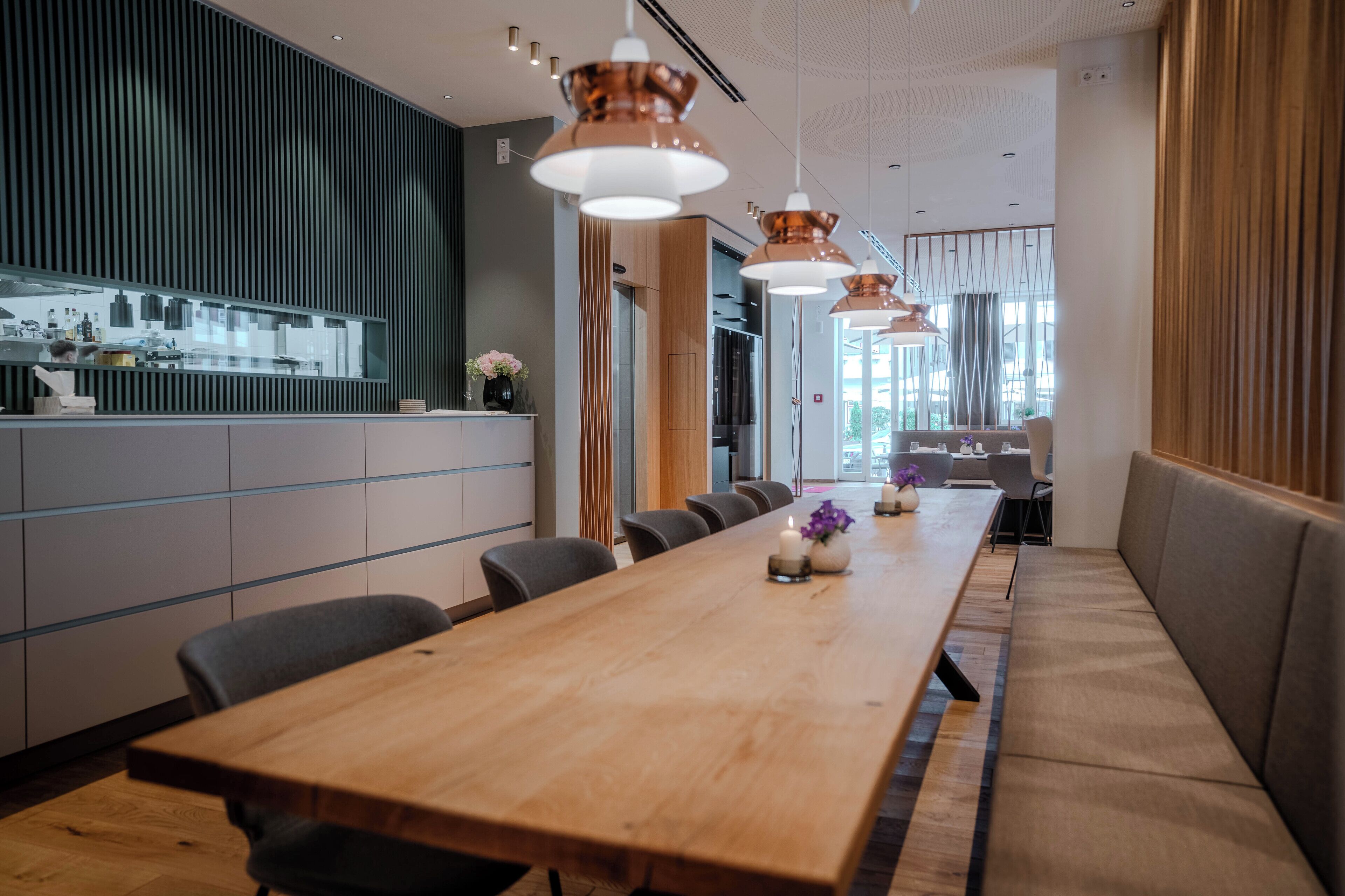 A modern dining area with a long wooden table, multiple chairs, and pendant lighting.