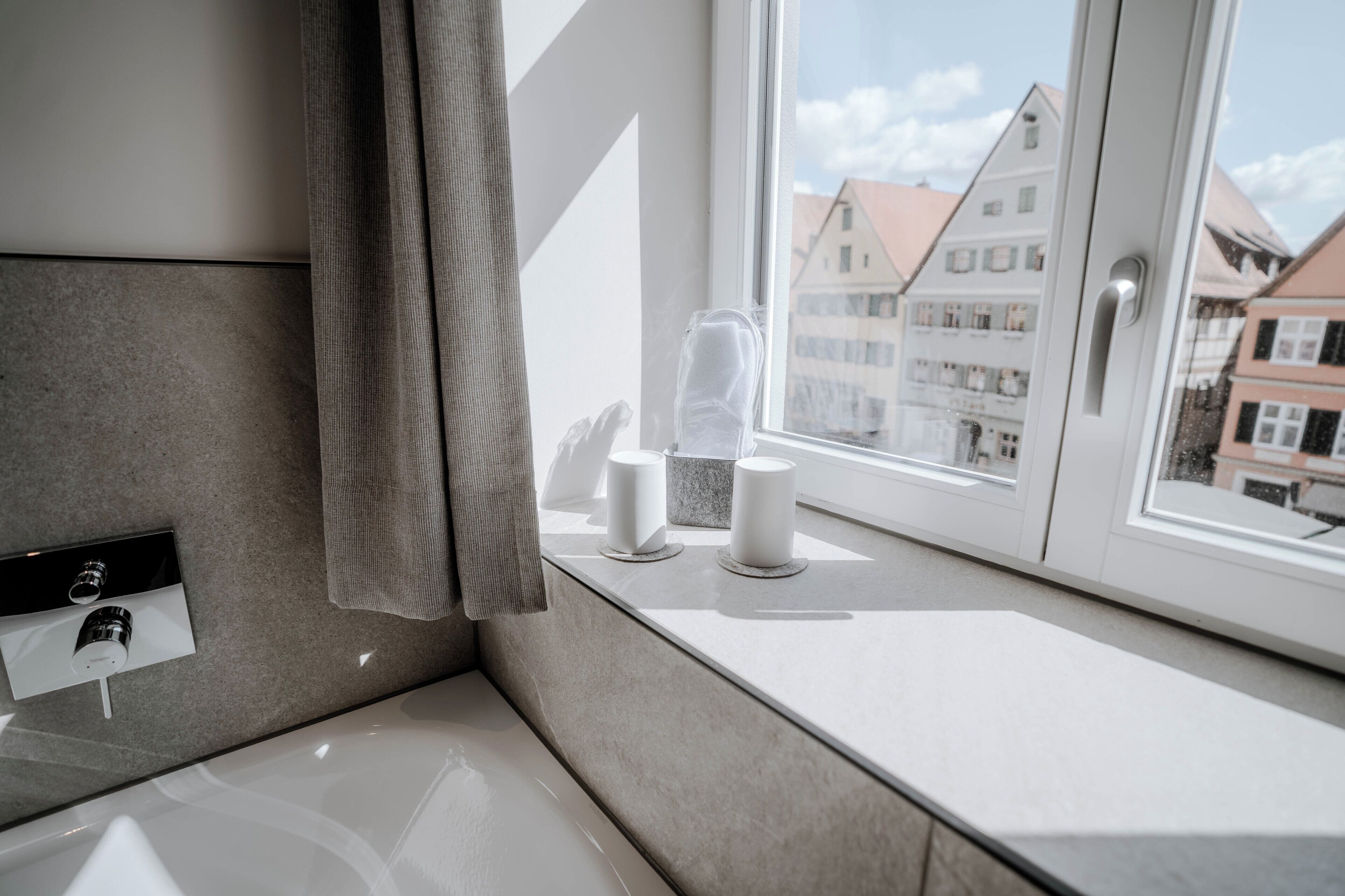 Une salle de bain moderne avec une baignoire, un distributeur de serviettes et une fenêtre donnant sur des immeubles.