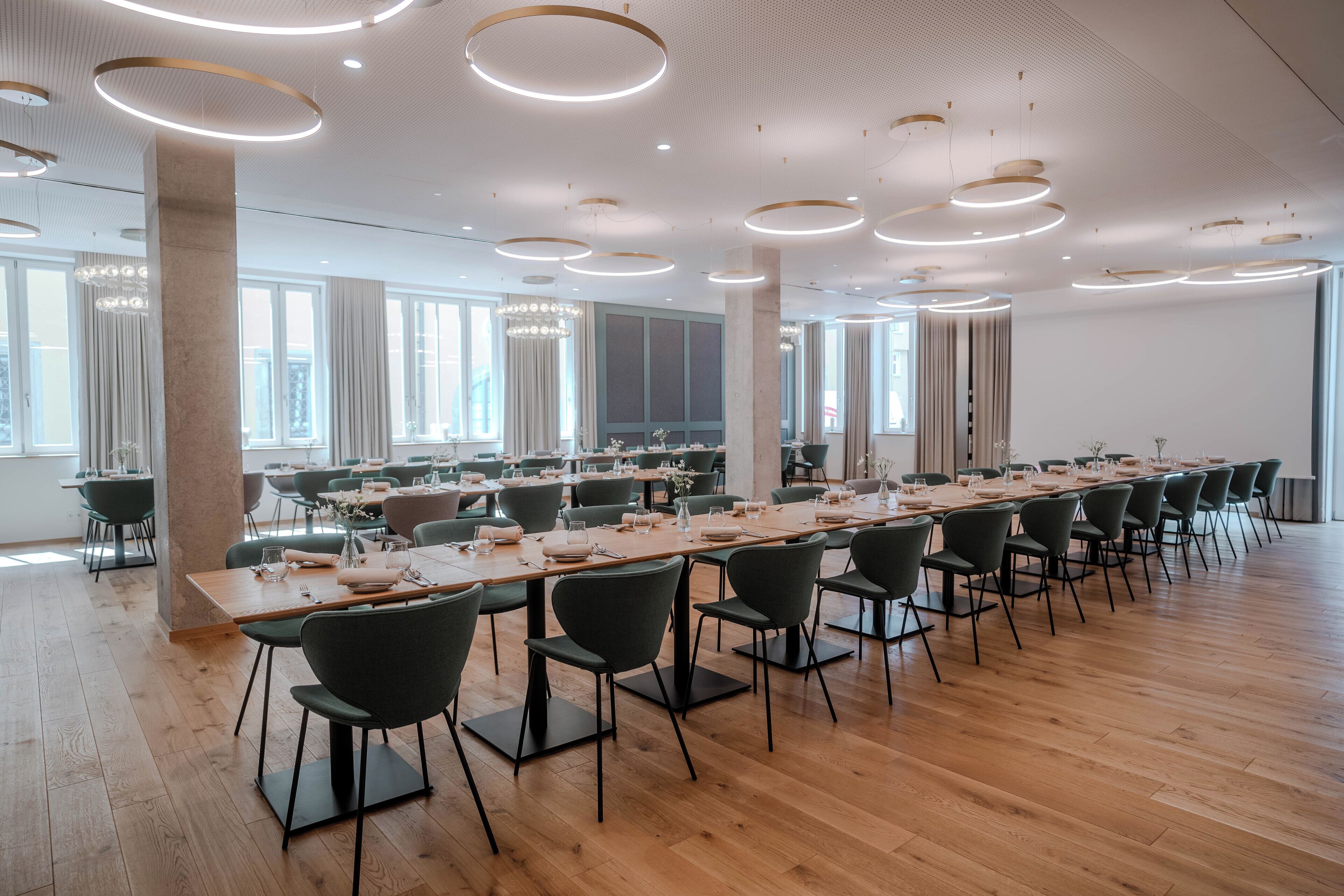 A spacious conference room with long tables, modern chairs, and circular ceiling lights.