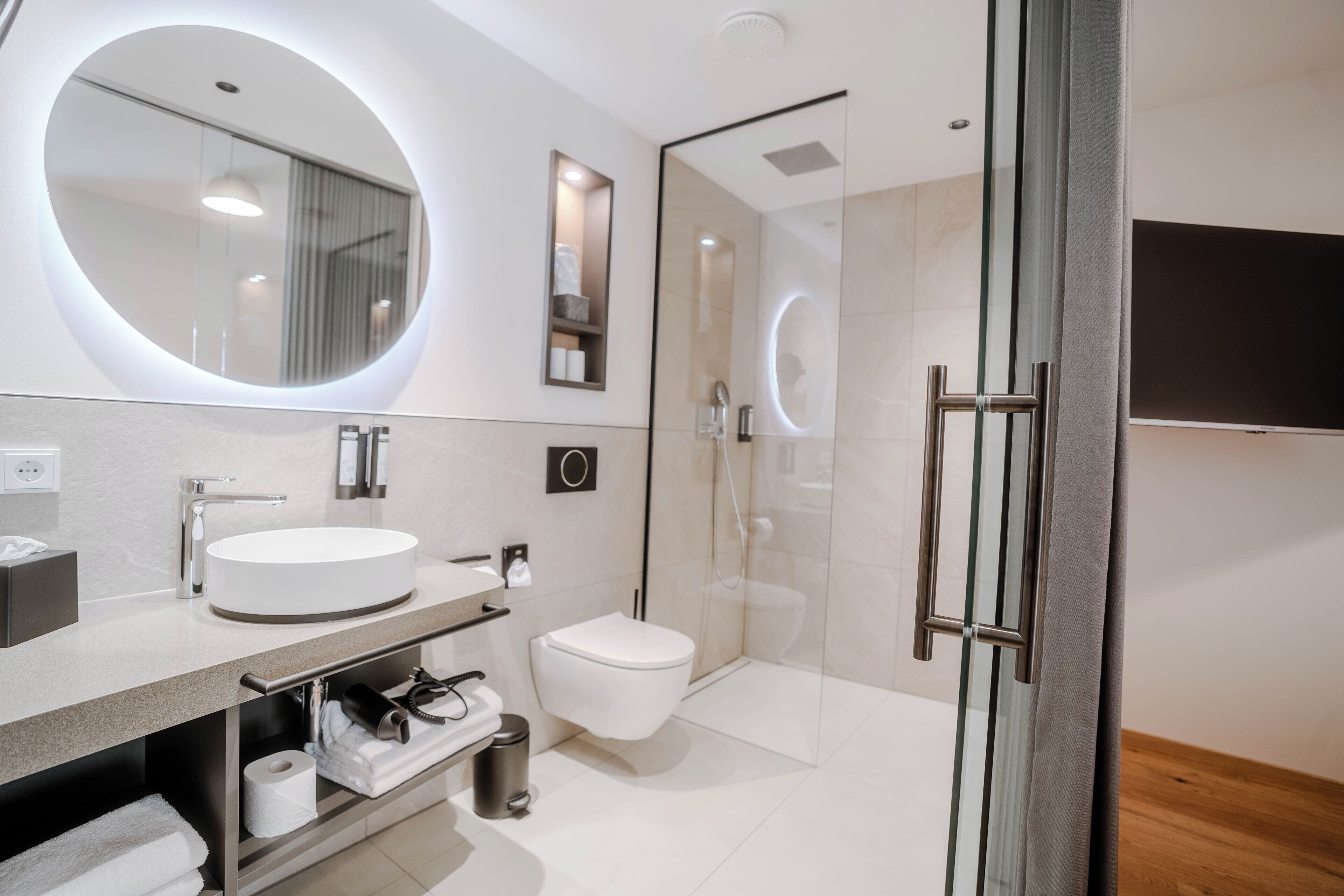 Ein modernes Badezimmer mit rundem Spiegel, Waschbecken, Toilette und Duschkabine.