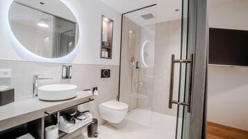 Ein modernes Badezimmer mit rundem Spiegel, Waschbecken, Toilette und Duschkabine.