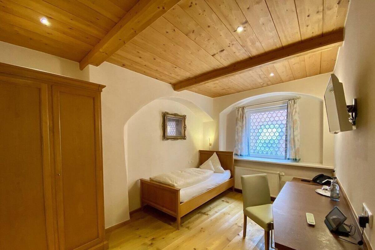 A bedroom with a wooden bed, a desk, a chair, a wardrobe, and a window with a view.