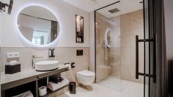A modern bathroom with a round mirror, a white sink, a toilet, and a glass-enclosed shower.
