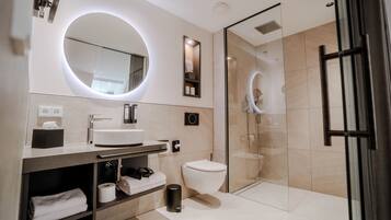 A modern bathroom with a round mirror, a toilet, a glass-enclosed shower, and a vanity with a sink and towel storage.
