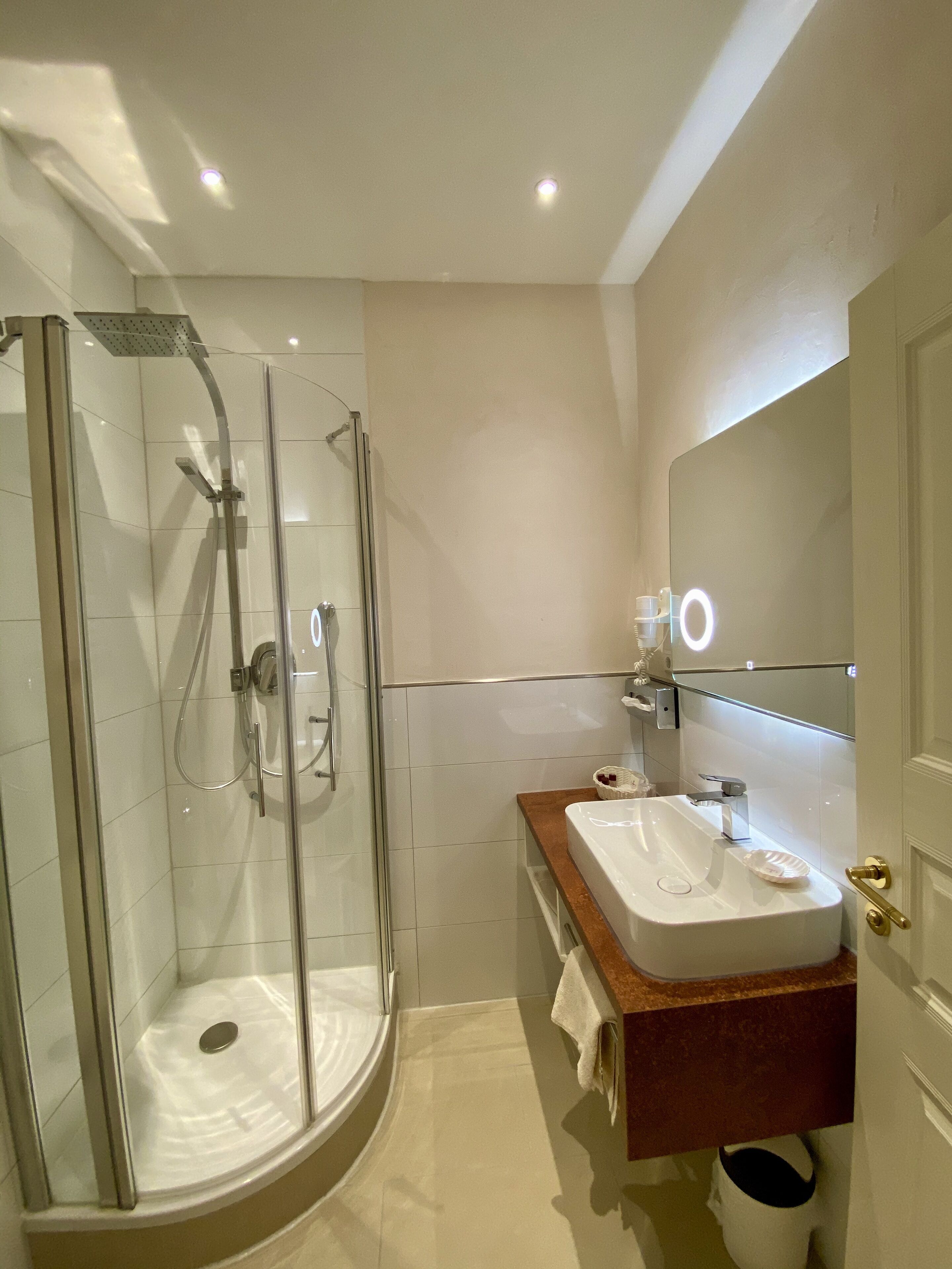 Une salle de bain moderne avec une douche à parois de verre, un lavabo blanc doté d’un plan de toilette en bois et un grand miroir.