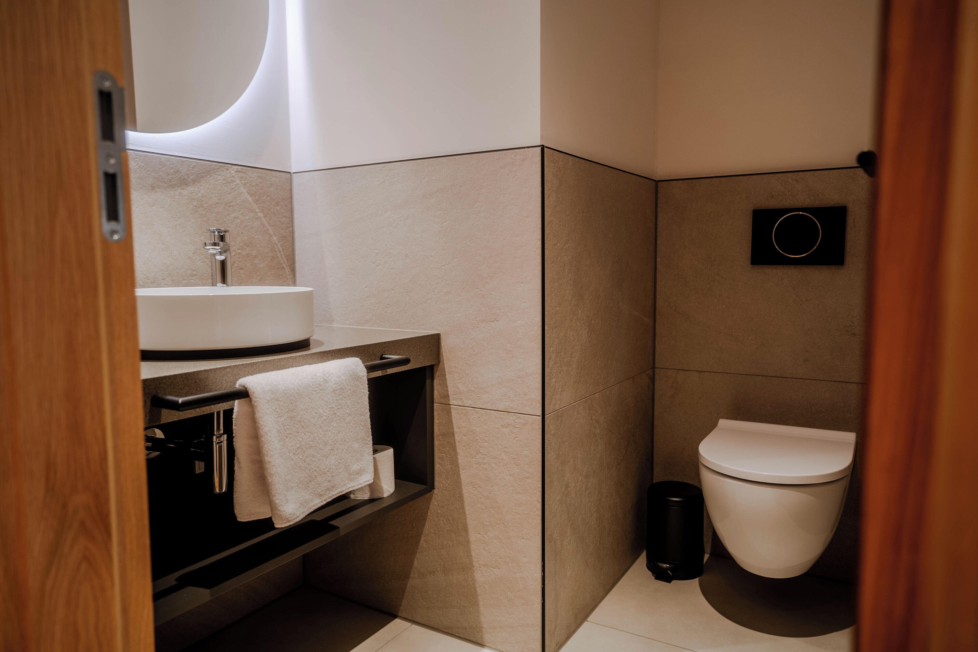 A modern bathroom with a sink, mirror, toilet, and trash can.