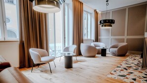 Une chambre d’hôtel moderne avec un plancher en bois, une table basse ronde et deux fauteuils blancs.