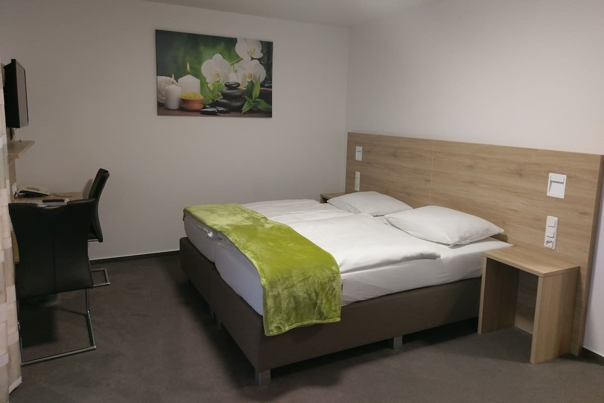 Ein Hotelzimmer mit Bett, Nachttisch, Schreibtisch mit Stuhl und einem Bild an der Wand.