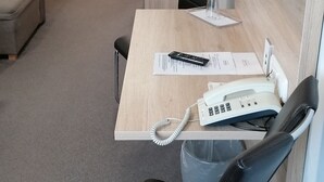 A modern office space with a desk, two chairs, a computer monitor, a telephone, and a trash bin. - Gasthaus Pension Rezatgrund (Windsbach)