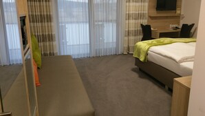 A hotel room with a bed, a bench, a desk, a TV, and a window with curtains. - Gasthaus Pension Rezatgrund (Windsbach)