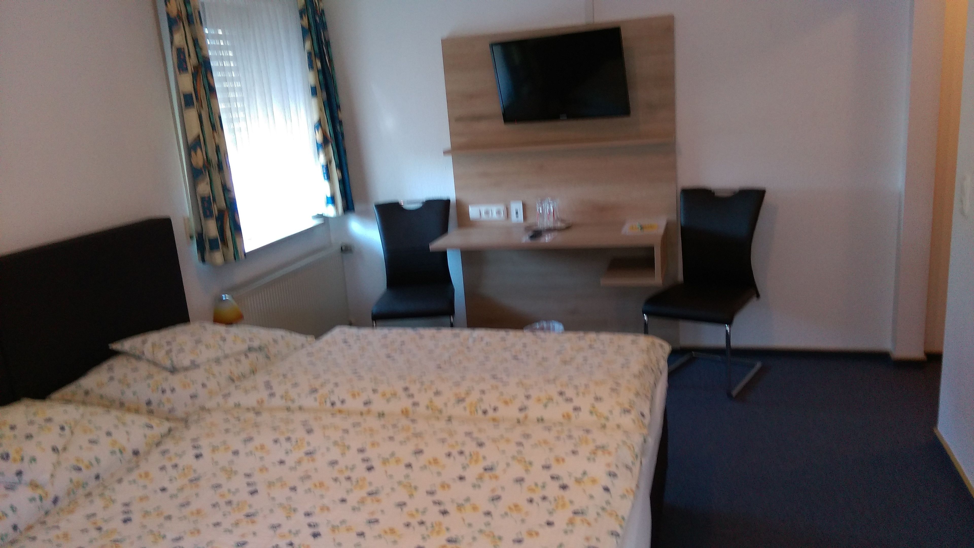 Une chambre d’hôtel comprenant un lit, un bureau avec un téléviseur à écran plat, deux chaises et une fenêtre avec des rideaux.