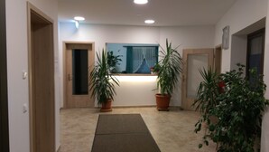 A hallway with a reception desk, two potted plants, a mat, and a door on the right. - Gasthaus Pension Rezatgrund (Windsbach)