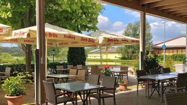 An outdoor patio area with tables and chairs under umbrellas, surrounded by greenery and a building in the background. - Gasthaus Pension Rezatgrund (Windsbach)