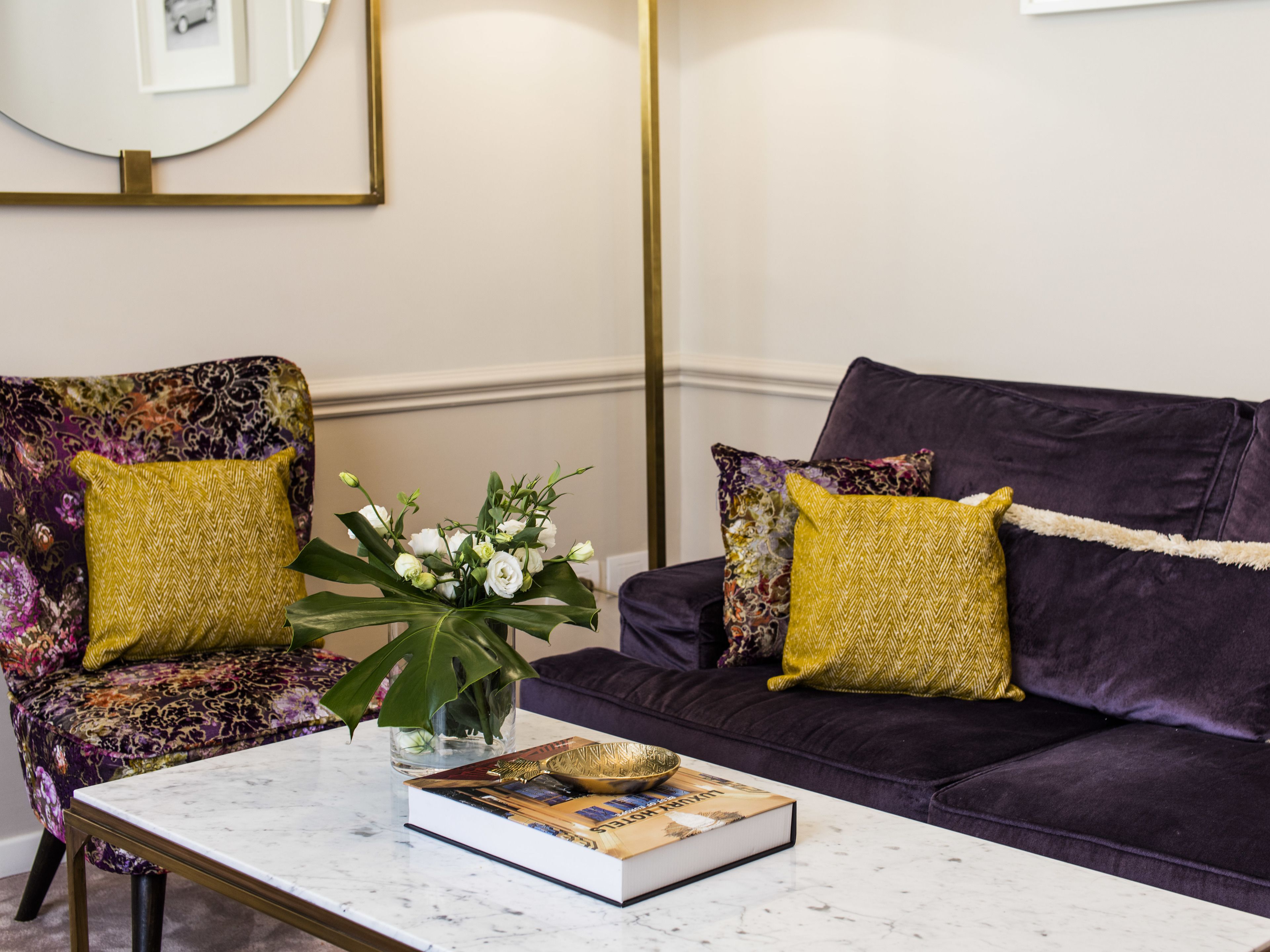 Una sala de estar con un sofá y un sillón, una mesita de centro con un libro y un cuenco decorativo, y un jarrón con flores.