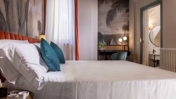Habitación de hotel con una cama grande, un escritorio con una silla, una mesita con una bandeja y una taza, y un mural grande en la pared.
