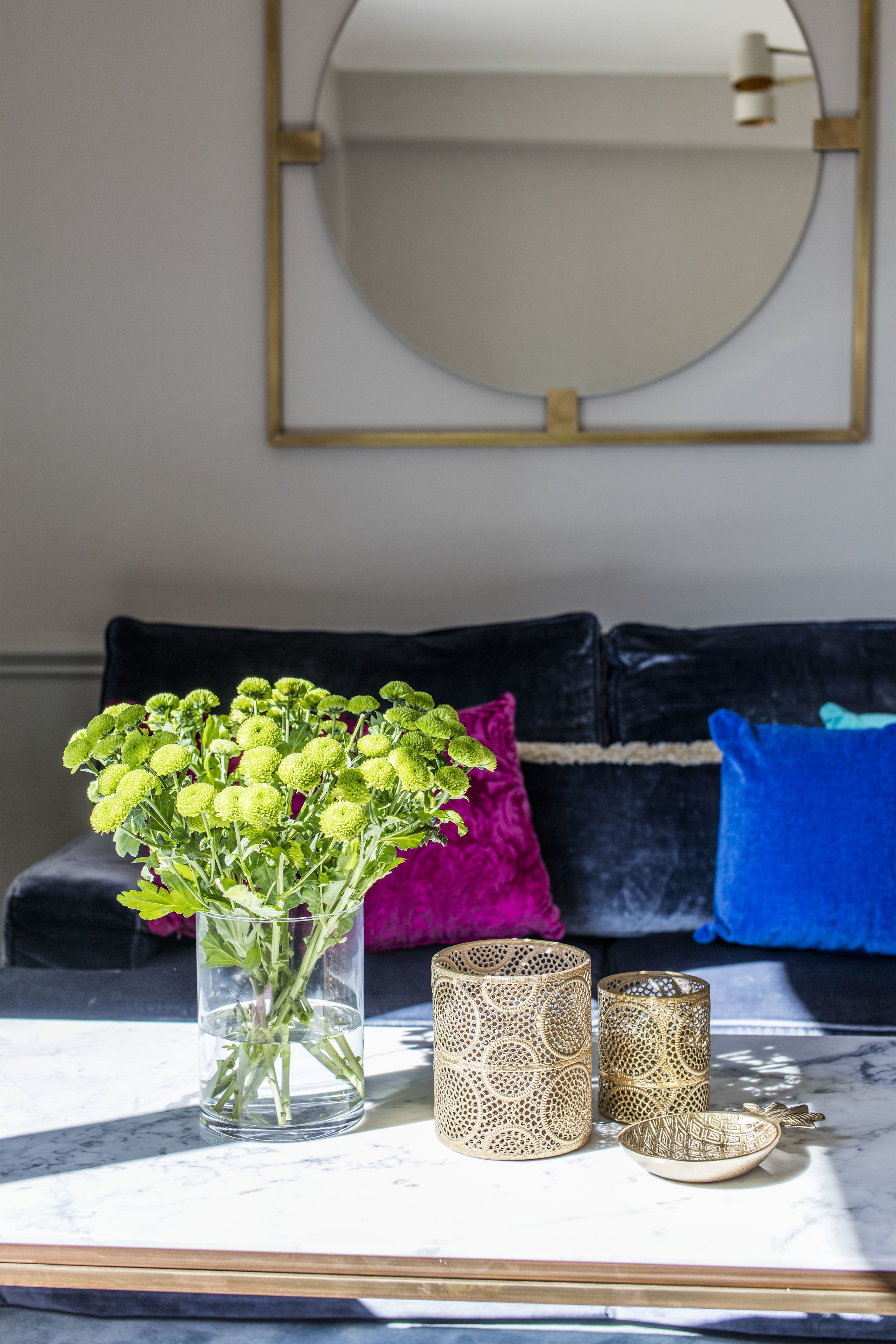 Een tafel met een vaas groene bloemen, twee sierlijke kandelaars en een kleine schaal.