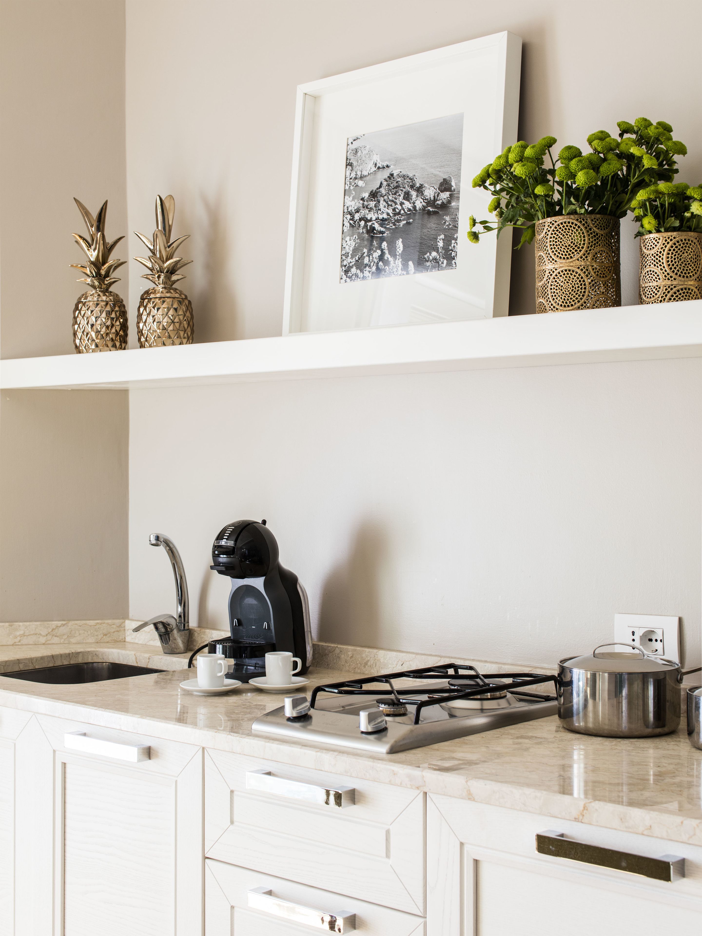 A kitchen with a coffee maker, a gas stove, and a sink. There are decorative pineapples and a framed picture on the shelf.