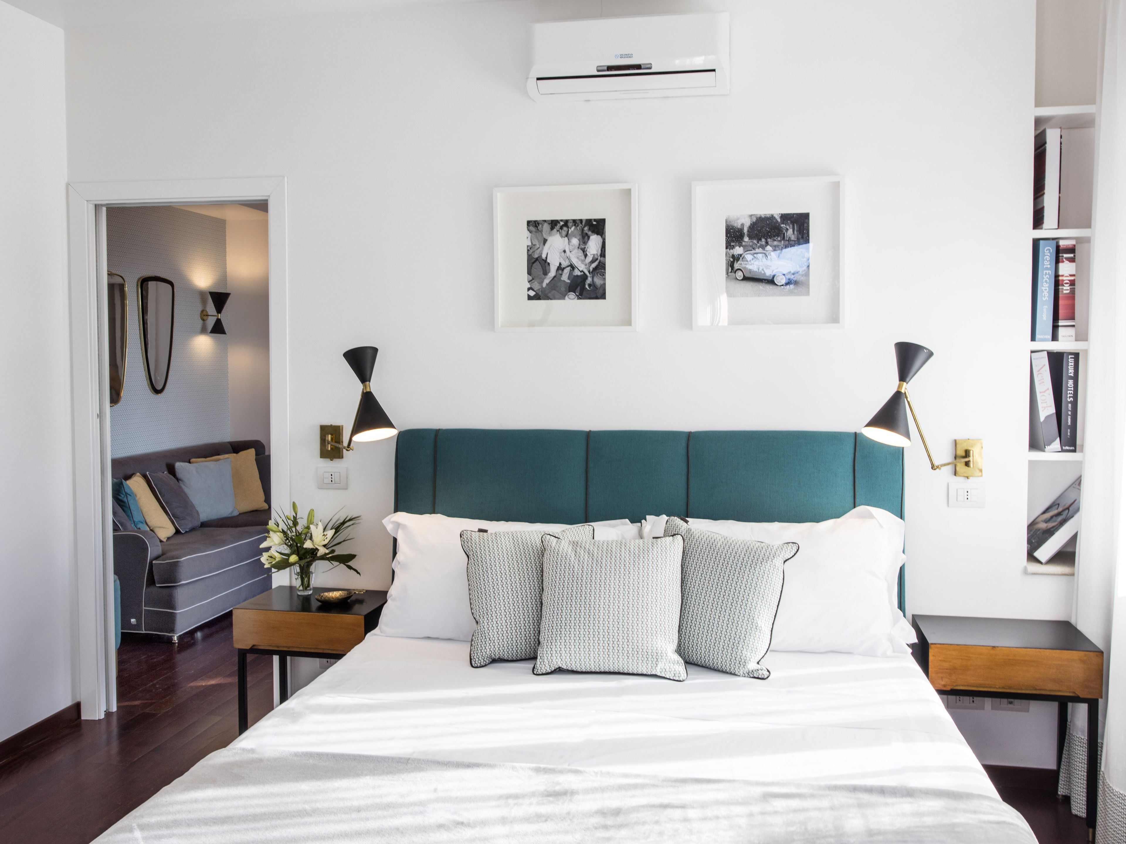 A modern bedroom with a teal headboard, white bedding, and two framed photographs on the wall.