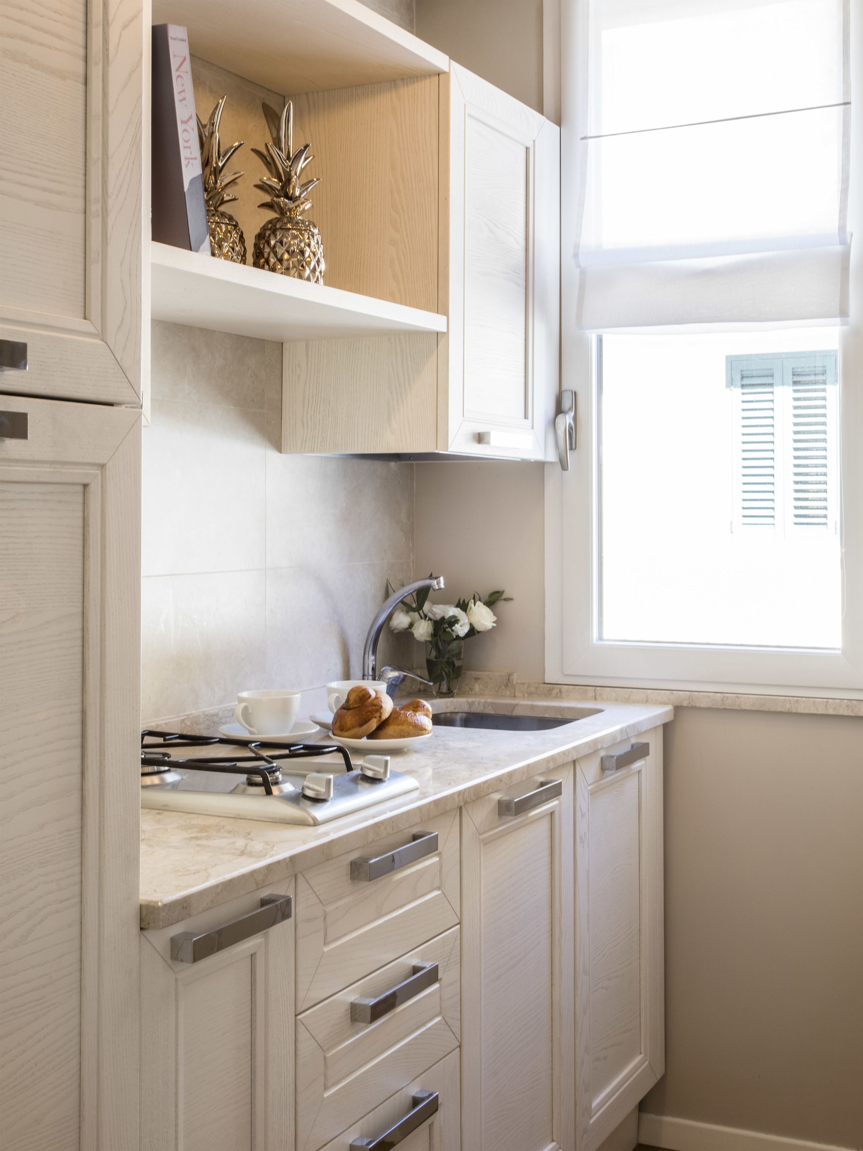 A kitchen with white cabinets, a marble countertop, a sink, and a window with blinds.