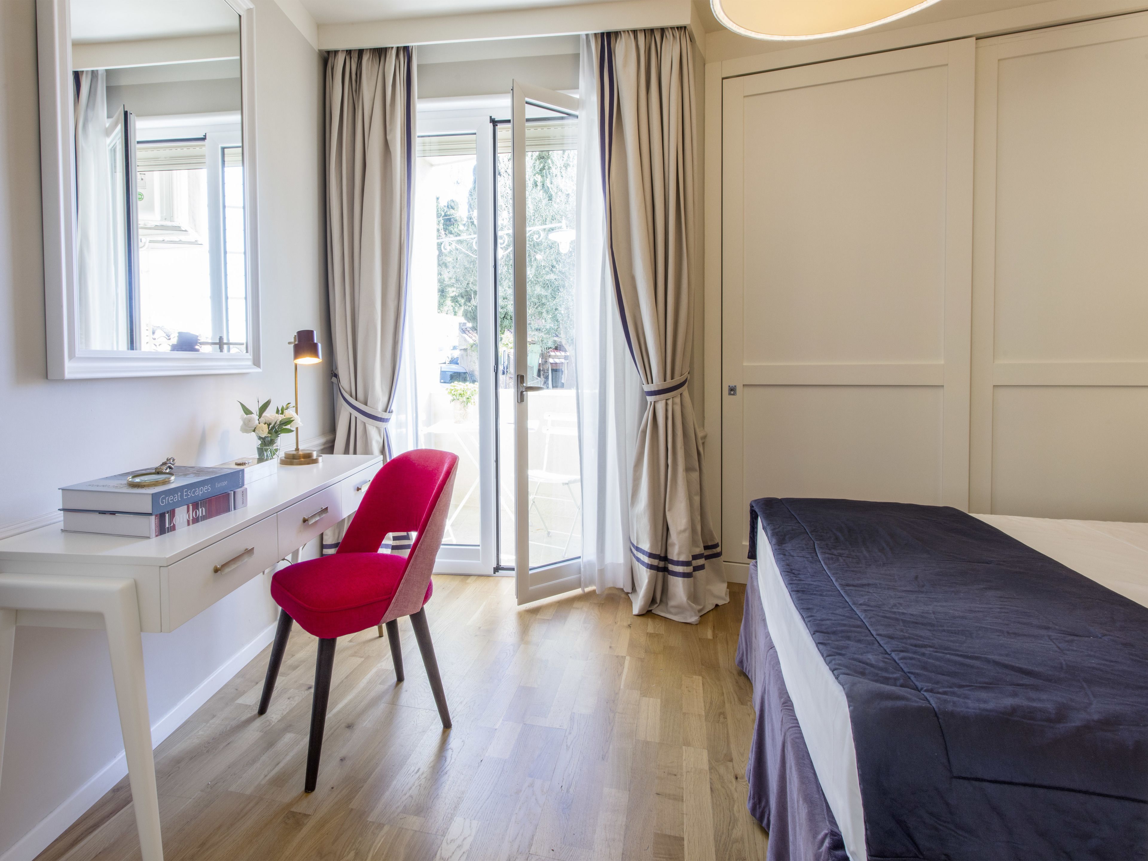 A bedroom with a bed, a desk, a chair, and a window with curtains.