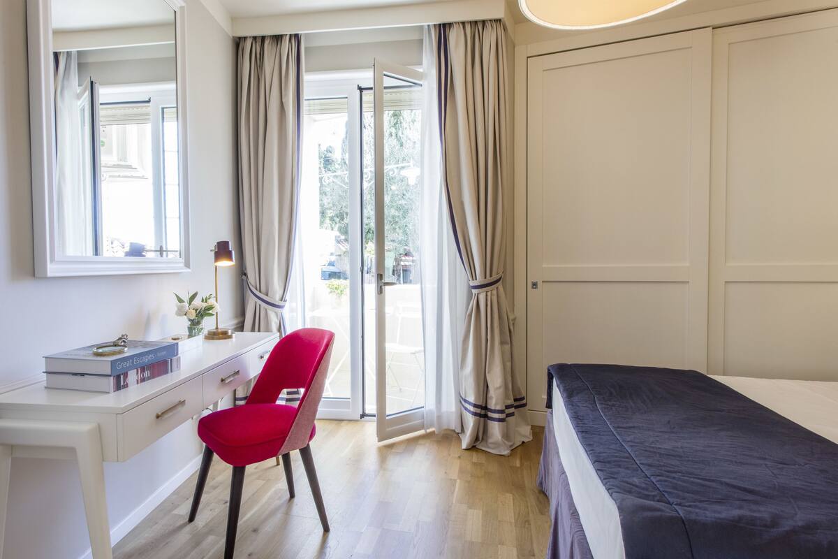 Une chambre à coucher avec un lit, un bureau, une chaise et une fenêtre avec des rideaux.