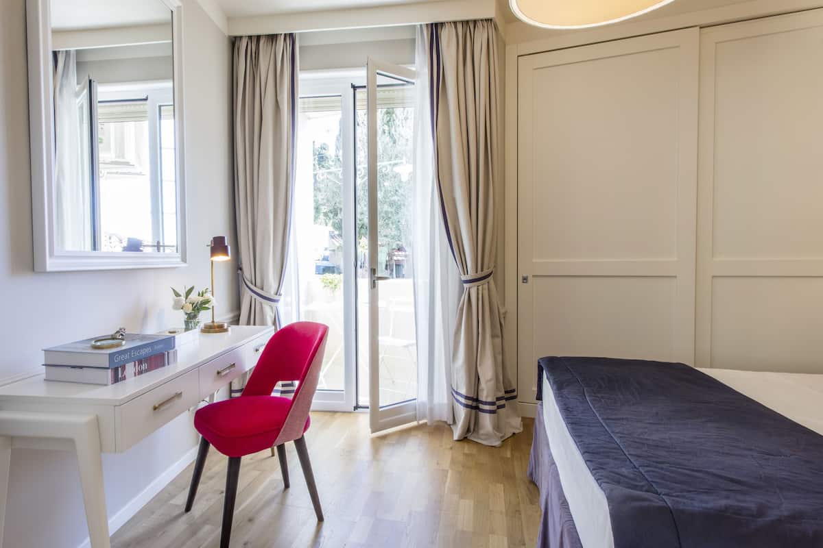 A bedroom with a bed, a desk, a chair, and a window with curtains.