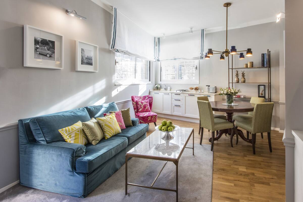 Un salon moderne avec un canapé bleu, une table basse en verre et un coin repas comprenant une table et des chaises en bois.