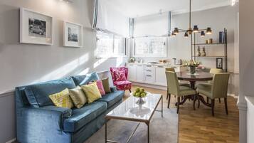 A modern living room with a blue sofa, a glass coffee table, and a dining area with a wooden table and chairs.