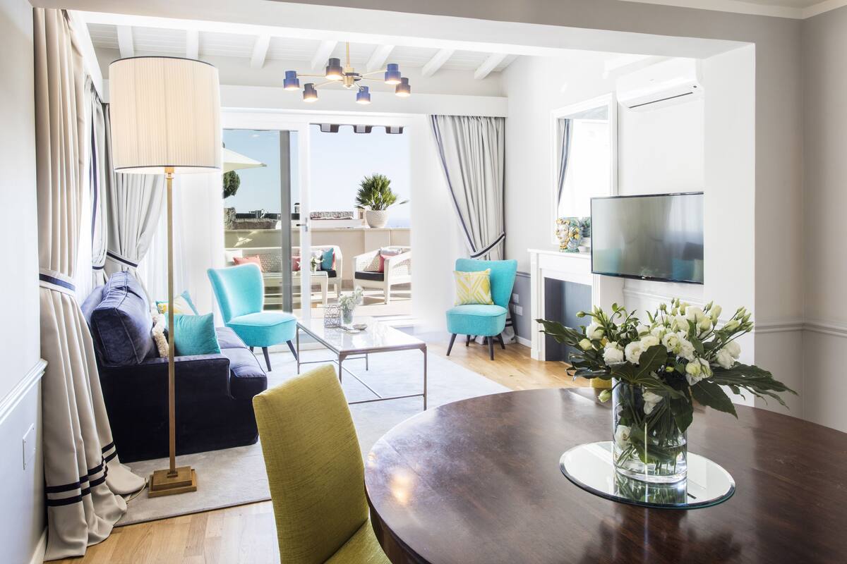 Un salon moderne avec une table ronde en bois, un lampadaire et un téléviseur fixé au mur. Il y a un balcon avec vue sur la ville.