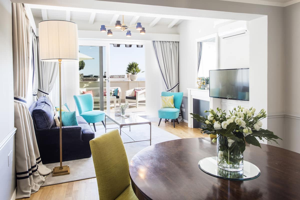 A modern living room with a round table, a sofa, and a TV. There is a balcony with a view of the city.