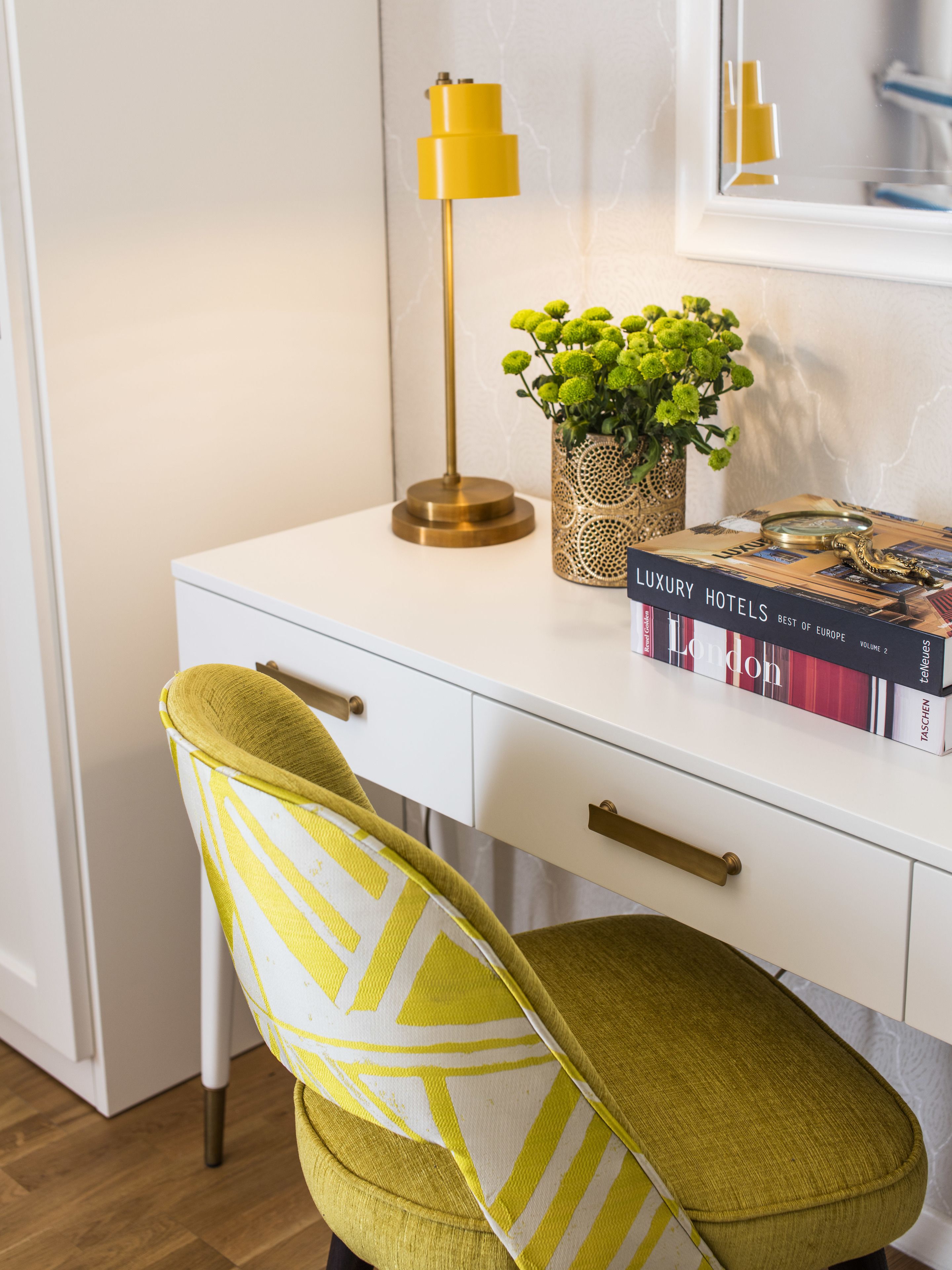 Un bureau blanc avec une lampe dorée, une plante en pot et un livre intitulé « Les meilleurs hôtels de luxe d’Europe, volume 2 ».