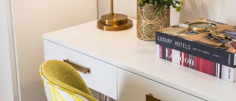 A white desk with a gold lamp, a potted plant, and a book titled "Luxury Hotels Best of Europe Volume 2".