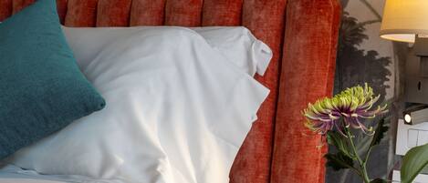 Una cama con almohadas blancas y turquesas, un cabecero rojo y un florero con una flor.