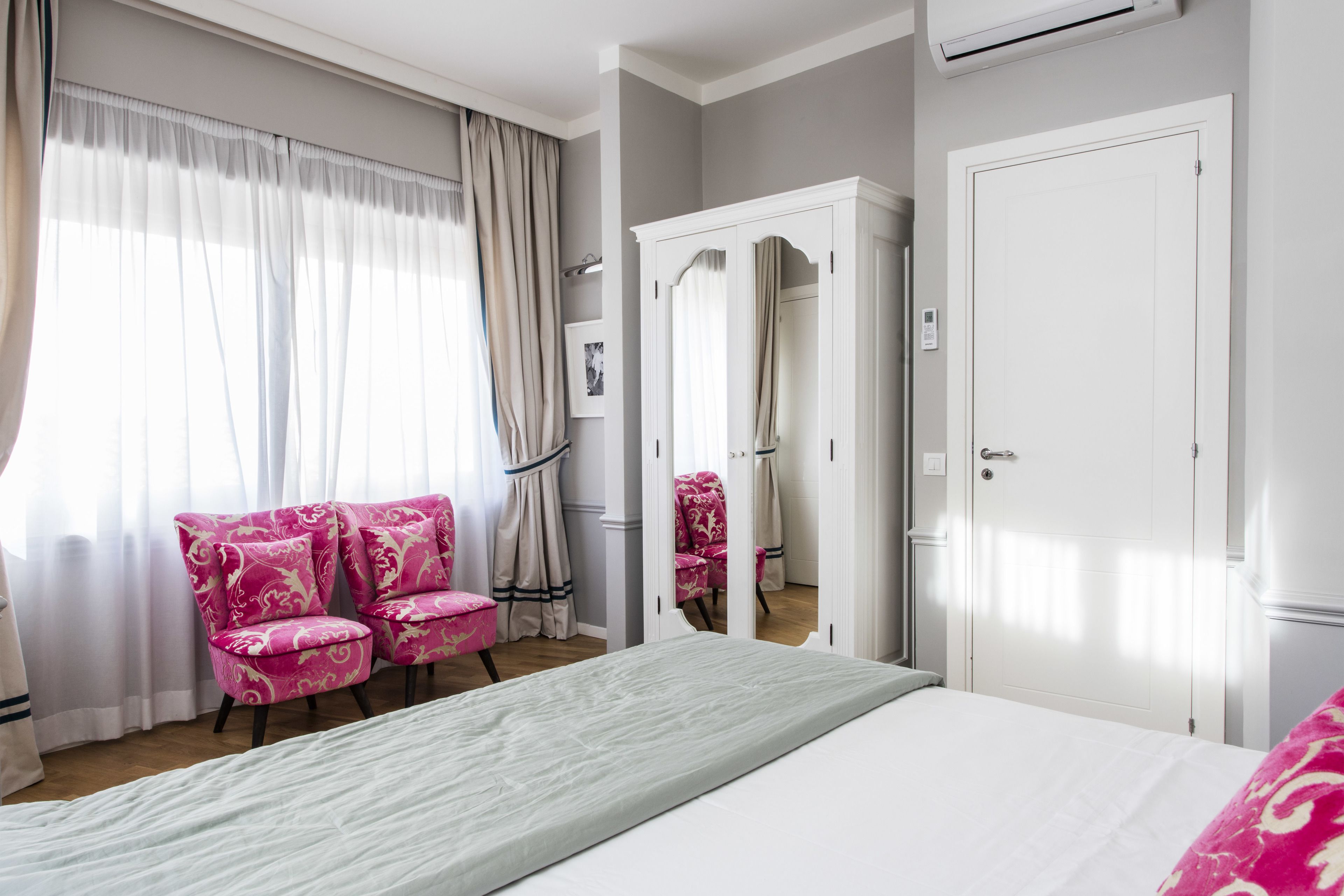 Quarto com cama, guarda-roupa e duas cadeiras cor-de-rosa.