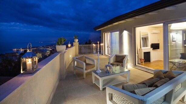 Ein Balkon mit Sitzgelegenheit, einem Glastisch und Blick auf die beleuchtete Stadt.
