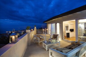 Un balcon avec des sièges d’extérieur, une table en verre et une vue sur la ville la nuit.
